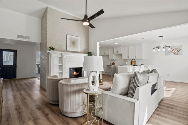 living room featuring a fireplace, high vaulted ceiling, light hardwood / wood-style flooring, and ceiling fan