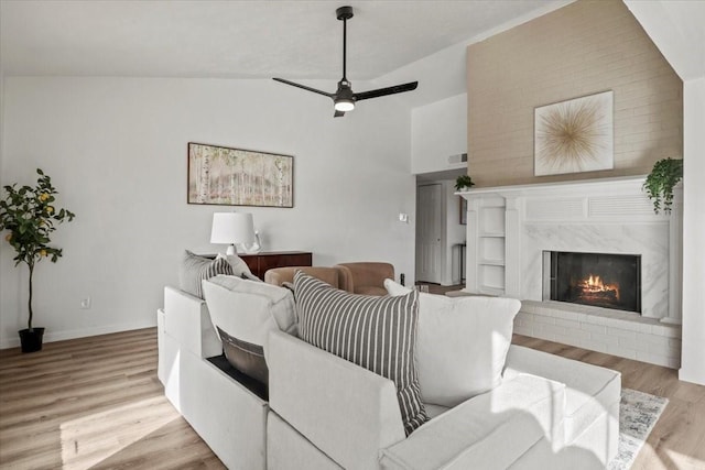 living room featuring a brick fireplace, light wood-type flooring, vaulted ceiling, and ceiling fan