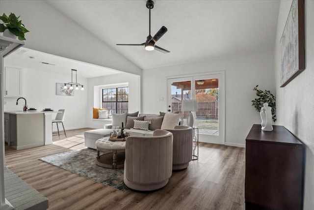 living room with ceiling fan with notable chandelier, hardwood / wood-style flooring, vaulted ceiling, and plenty of natural light