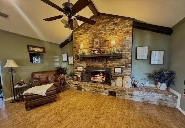 living room featuring a brick fireplace, ornamental molding, lofted ceiling with beams, and ceiling fan