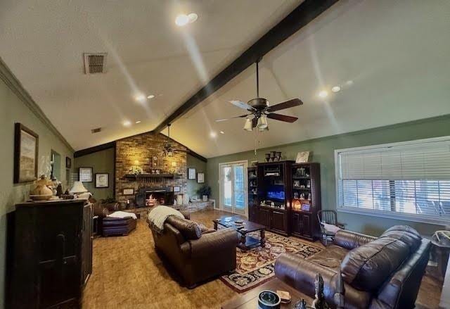 living room with vaulted ceiling with beams, a healthy amount of sunlight, a stone fireplace, and ceiling fan