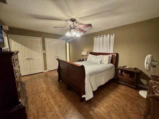 bedroom with a textured ceiling, ceiling fan, dark hardwood / wood-style floors, and two closets