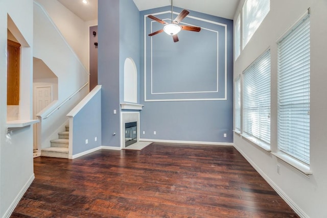 unfurnished living room featuring dark hardwood / wood-style flooring, high vaulted ceiling, ceiling fan, and a tiled fireplace