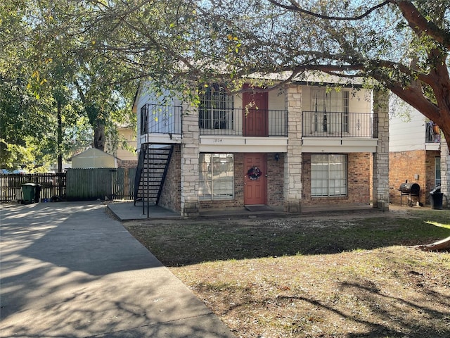 view of front of property featuring brick siding, stairs, a balcony, and fence