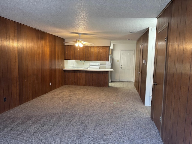 kitchen with light carpet, wooden walls, a peninsula, and a textured ceiling