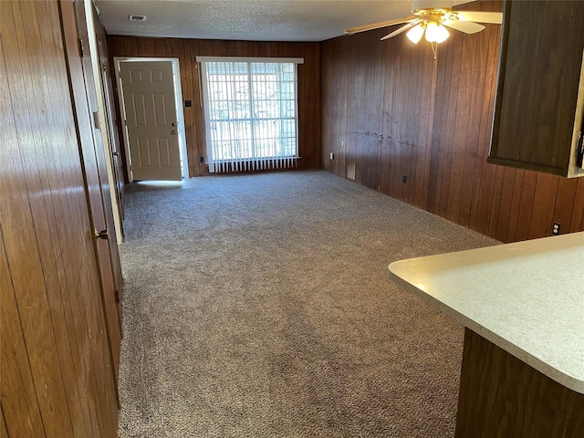 spare room featuring a ceiling fan, carpet, wooden walls, and a textured ceiling