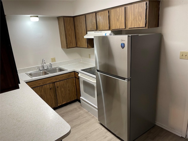 kitchen with light wood finished floors, white range with electric cooktop, under cabinet range hood, freestanding refrigerator, and a sink