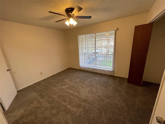 unfurnished bedroom featuring baseboards, a textured ceiling, a ceiling fan, and dark colored carpet