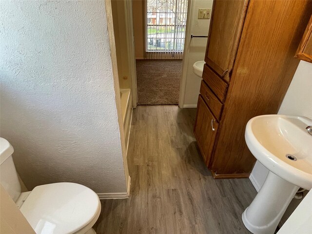 full bath featuring toilet, wood finished floors, baseboards, and a textured wall