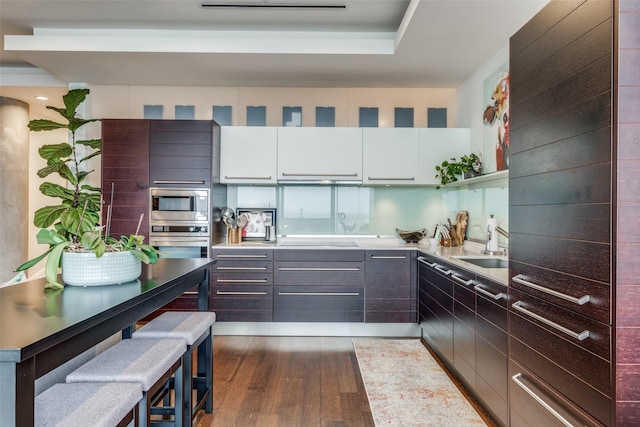 kitchen featuring a breakfast bar, stainless steel appliances, sink, dark hardwood / wood-style floors, and white cabinetry