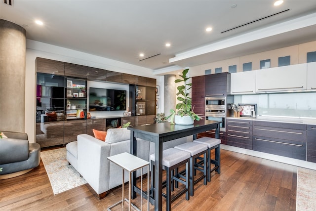 kitchen with stainless steel microwave, light wood-type flooring, white cabinetry, and dark brown cabinetry