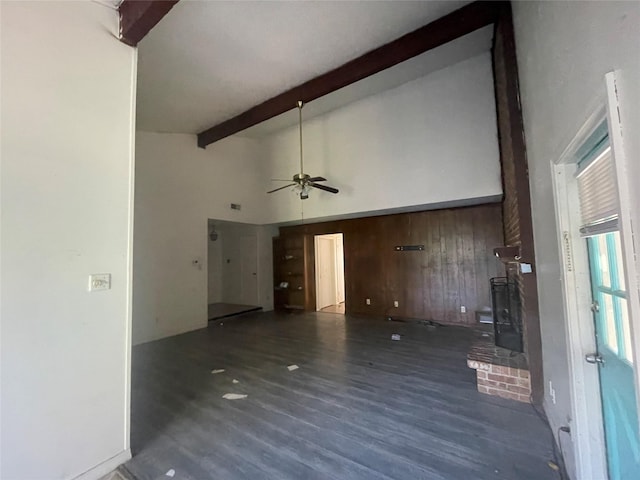 unfurnished living room with ceiling fan, high vaulted ceiling, dark hardwood / wood-style flooring, beamed ceiling, and wood walls