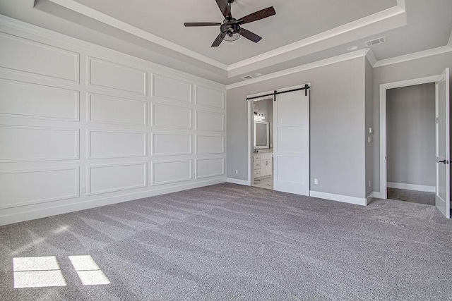 unfurnished bedroom featuring carpet, a tray ceiling, ceiling fan, a barn door, and connected bathroom