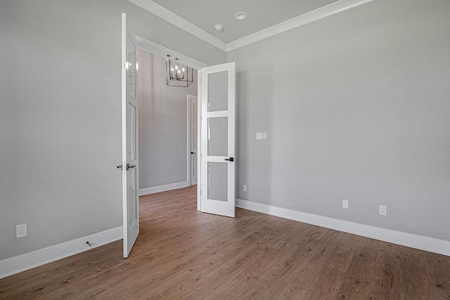 empty room with hardwood / wood-style floors, a notable chandelier, and ornamental molding