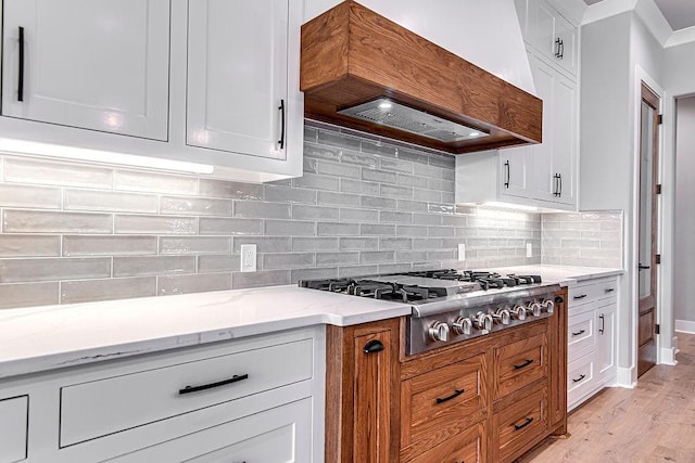 kitchen with premium range hood, light hardwood / wood-style flooring, light stone countertops, white cabinetry, and stainless steel gas cooktop