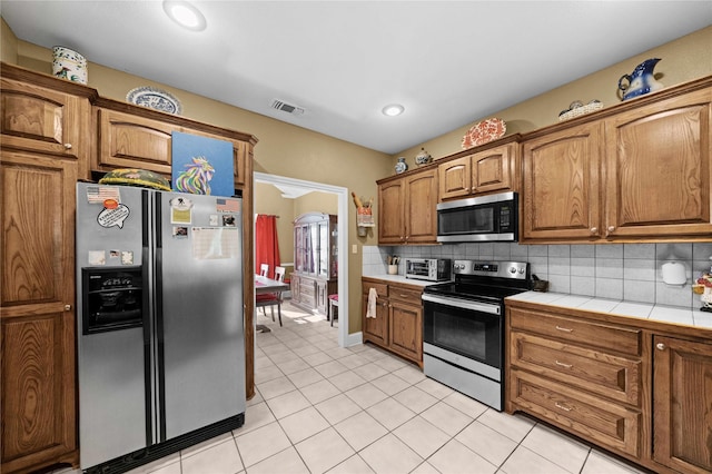 kitchen featuring tasteful backsplash, tile countertops, stainless steel appliances, and light tile patterned flooring