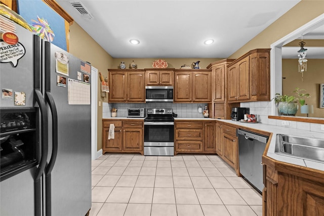 kitchen featuring light tile patterned floors, decorative backsplash, decorative light fixtures, and appliances with stainless steel finishes