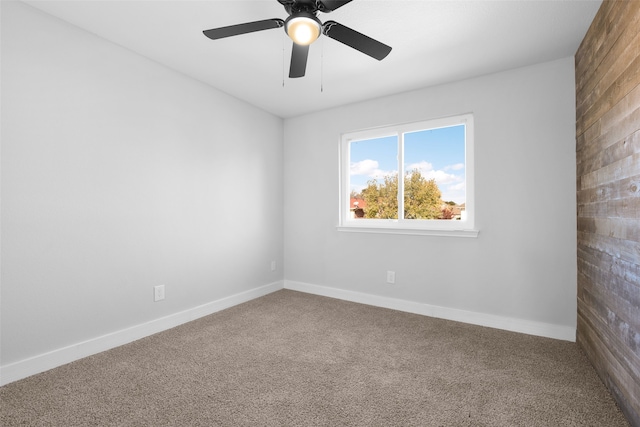 spare room with carpet floors, ceiling fan, and wood walls