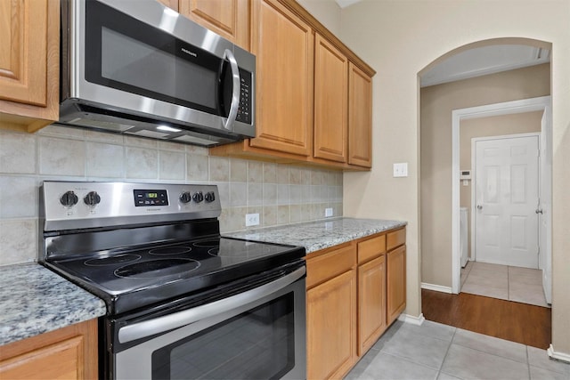 kitchen with appliances with stainless steel finishes, light tile patterned floors, light stone counters, and backsplash