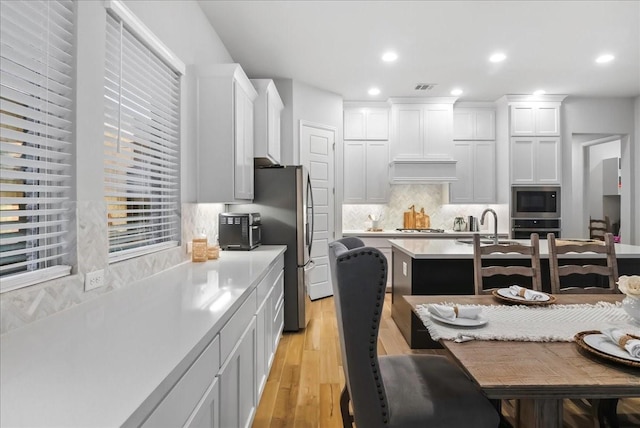 kitchen with custom exhaust hood, decorative backsplash, light wood-type flooring, appliances with stainless steel finishes, and white cabinetry