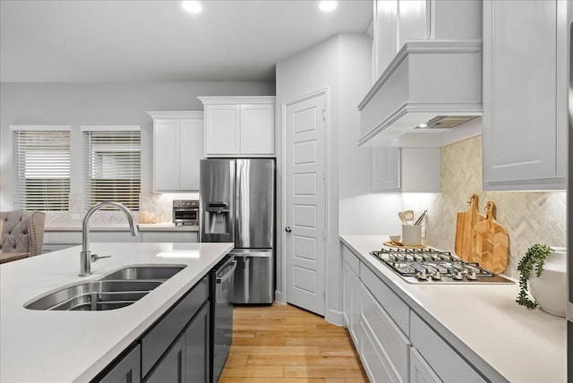 kitchen featuring backsplash, sink, light hardwood / wood-style flooring, white cabinetry, and stainless steel appliances