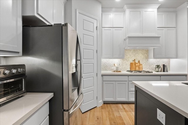 kitchen featuring backsplash, custom exhaust hood, stainless steel appliances, light hardwood / wood-style flooring, and white cabinets