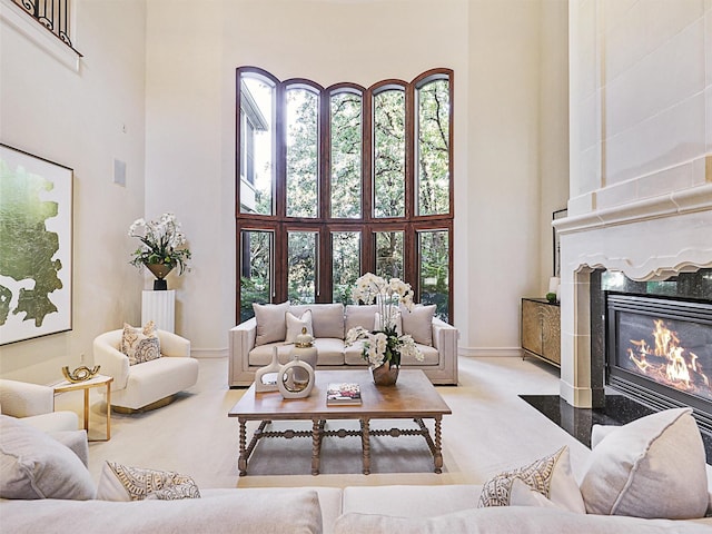 carpeted living room featuring a high end fireplace and a high ceiling