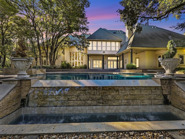 pool at dusk featuring ceiling fan and a jacuzzi