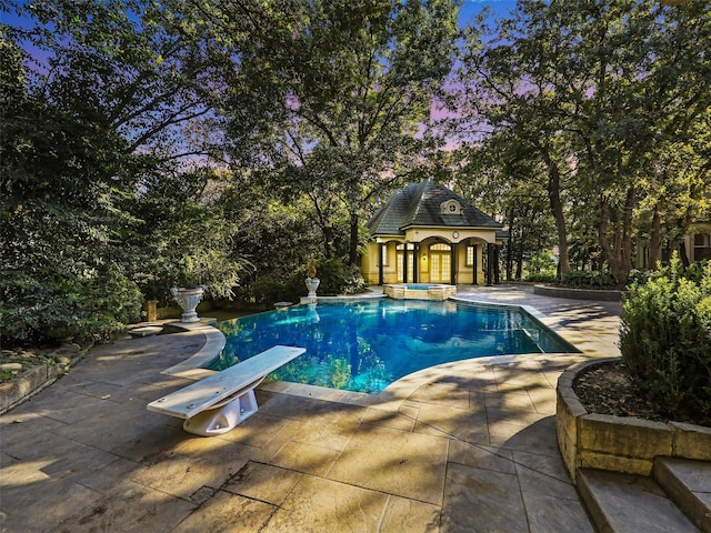 pool at dusk featuring a diving board, an outbuilding, and a patio