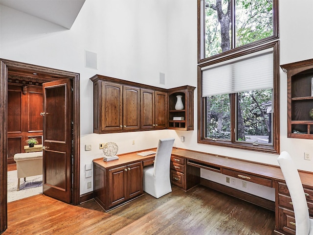 office area with a high ceiling, wood-type flooring, and built in desk