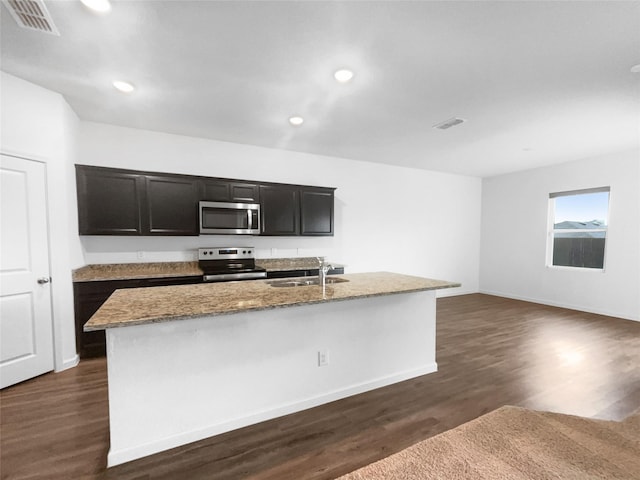 kitchen with stainless steel appliances, a kitchen island with sink, sink, and dark wood-type flooring