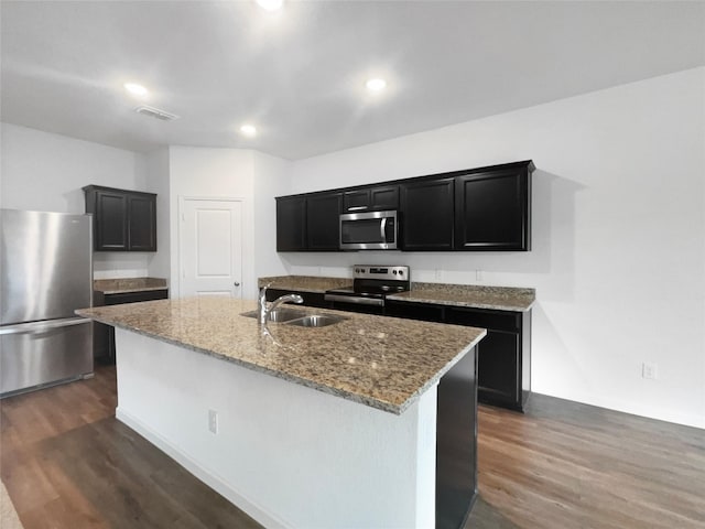 kitchen with sink, dark hardwood / wood-style floors, an island with sink, stainless steel appliances, and light stone countertops