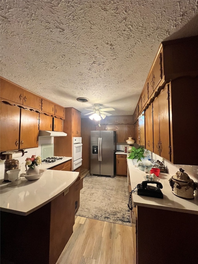 kitchen featuring stainless steel fridge with ice dispenser, light hardwood / wood-style flooring, ceiling fan, and a textured ceiling