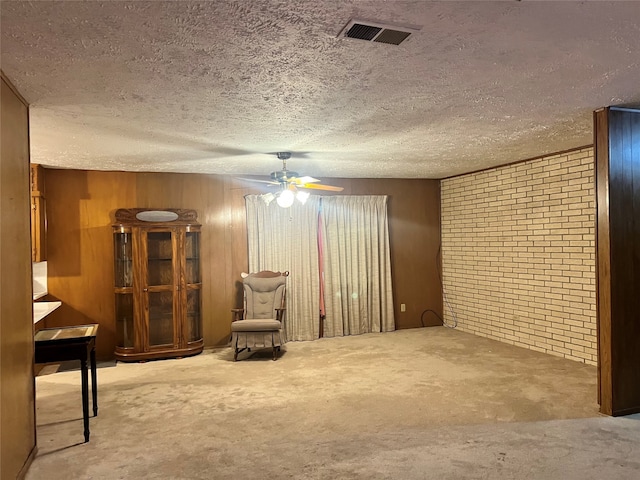 unfurnished room featuring a textured ceiling, ceiling fan, wood walls, and brick wall