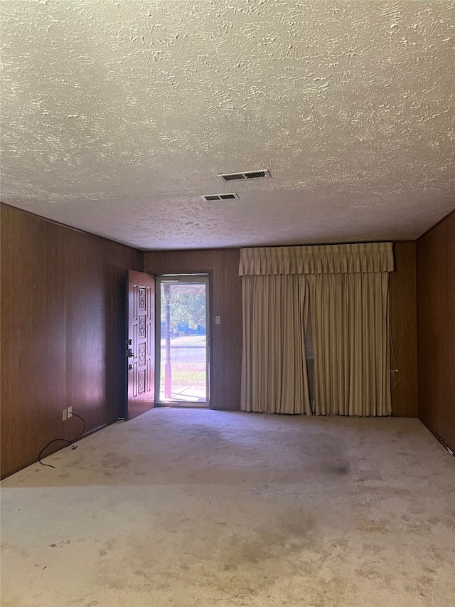 unfurnished room with wood walls, carpet floors, and a textured ceiling