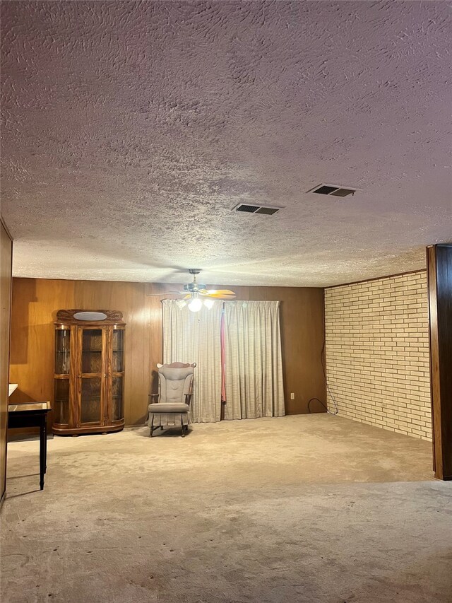 basement with ceiling fan, wooden walls, and a textured ceiling