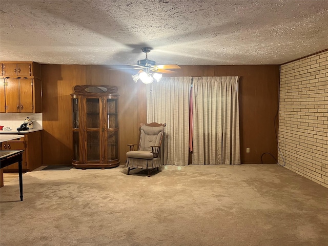 sitting room featuring light carpet, wooden walls, ceiling fan, a textured ceiling, and brick wall