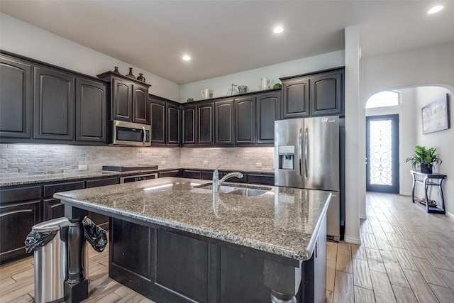 kitchen with appliances with stainless steel finishes, a center island with sink, light stone counters, and sink