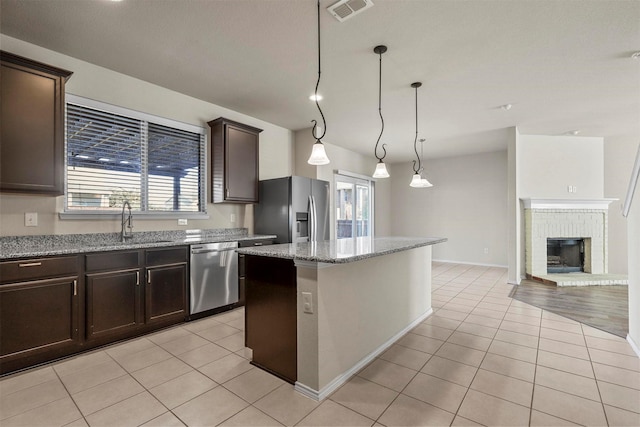 kitchen with light stone counters, decorative light fixtures, light tile patterned floors, appliances with stainless steel finishes, and a kitchen island