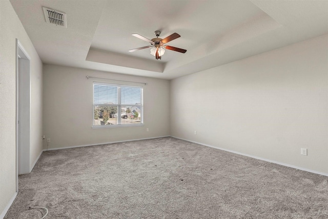 carpeted spare room with a raised ceiling and ceiling fan