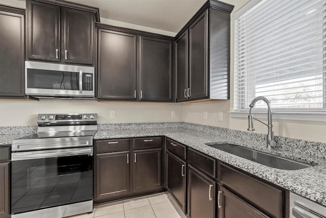 kitchen with sink, light tile patterned floors, light stone counters, stainless steel appliances, and dark brown cabinets