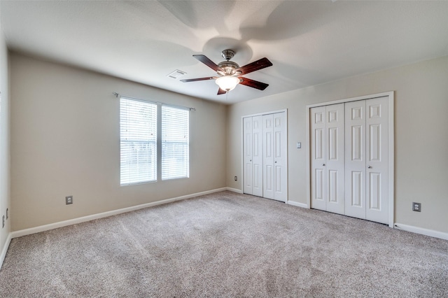 unfurnished bedroom featuring ceiling fan, light carpet, and multiple closets