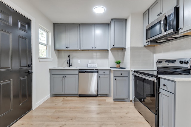 kitchen with stainless steel appliances, gray cabinetry, and light hardwood / wood-style floors