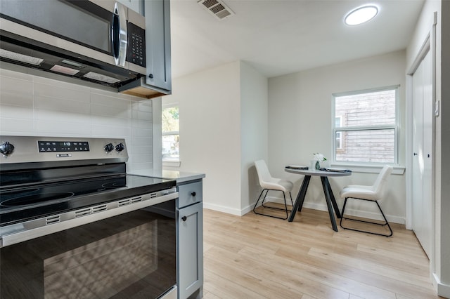 kitchen featuring gray cabinetry, backsplash, appliances with stainless steel finishes, and light hardwood / wood-style flooring