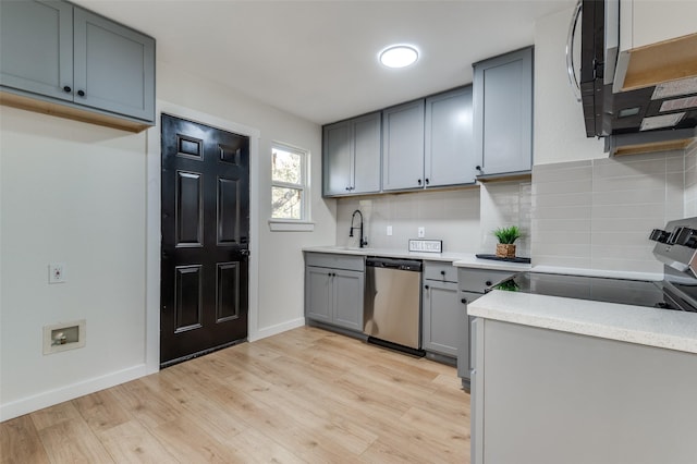 kitchen featuring gray cabinetry, decorative backsplash, stainless steel dishwasher, and light wood-type flooring