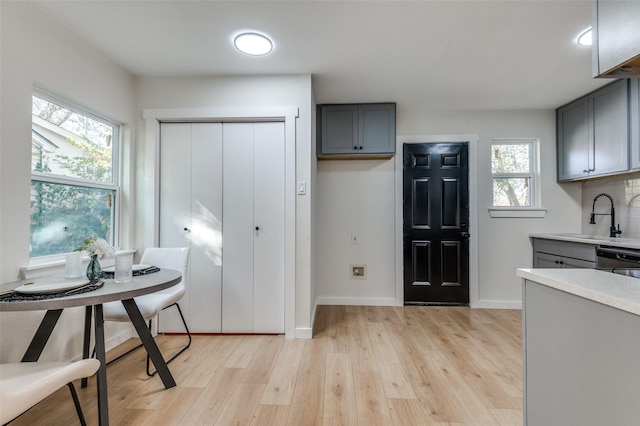 kitchen with gray cabinetry, light hardwood / wood-style floors, stainless steel dishwasher, and sink