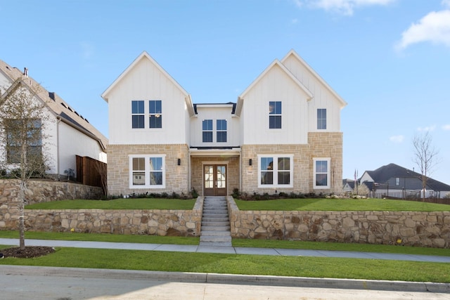 view of front of home with stone siding, fence, french doors, board and batten siding, and a front yard