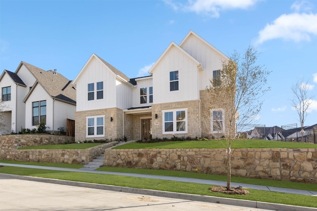 modern farmhouse featuring stone siding, a front lawn, and board and batten siding