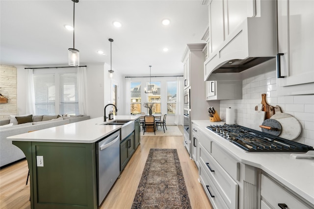 kitchen featuring a kitchen island with sink, under cabinet range hood, appliances with stainless steel finishes, green cabinets, and backsplash