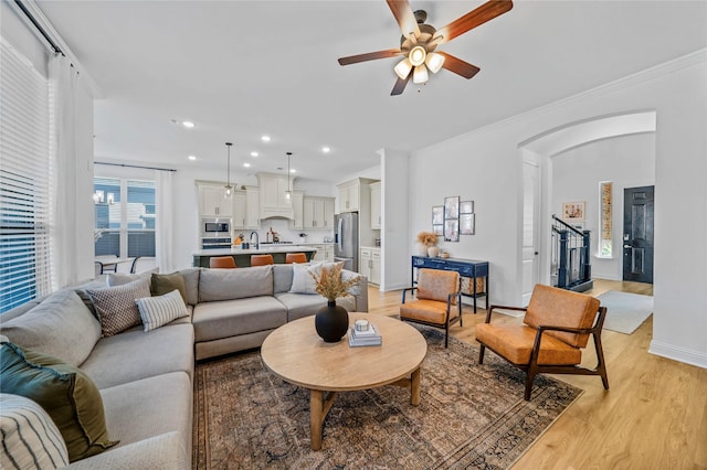 living room with crown molding, ceiling fan, recessed lighting, light wood-style flooring, and arched walkways